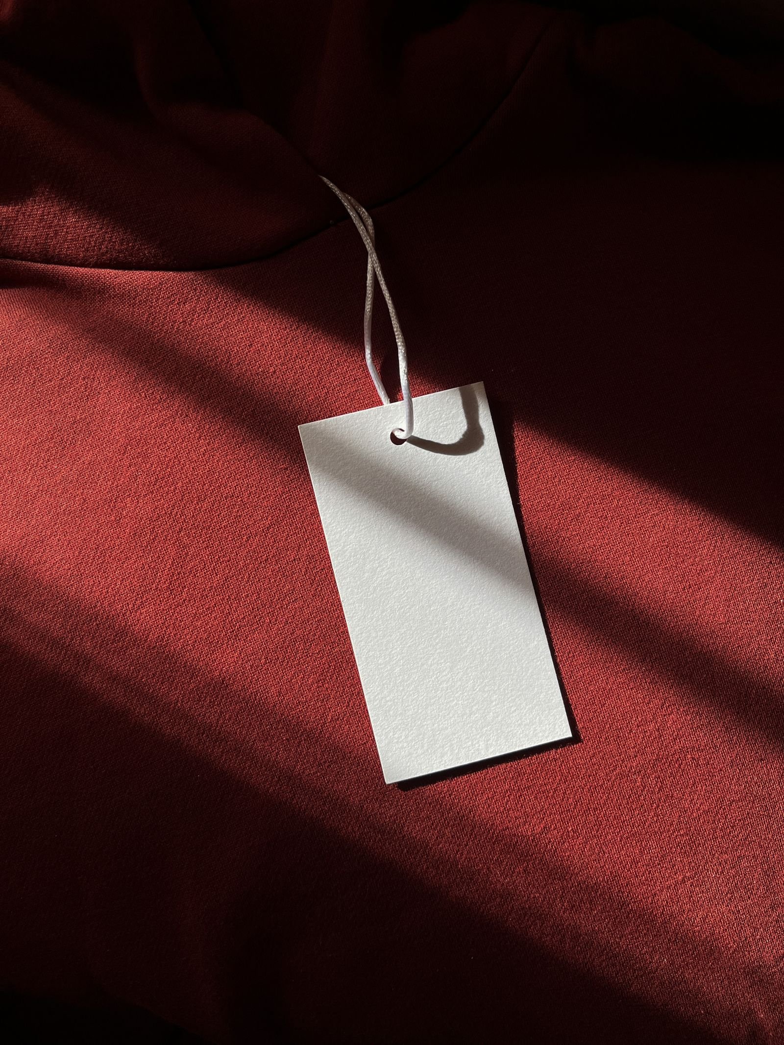 Blank paper hang tag attached to a red garment in sunlight