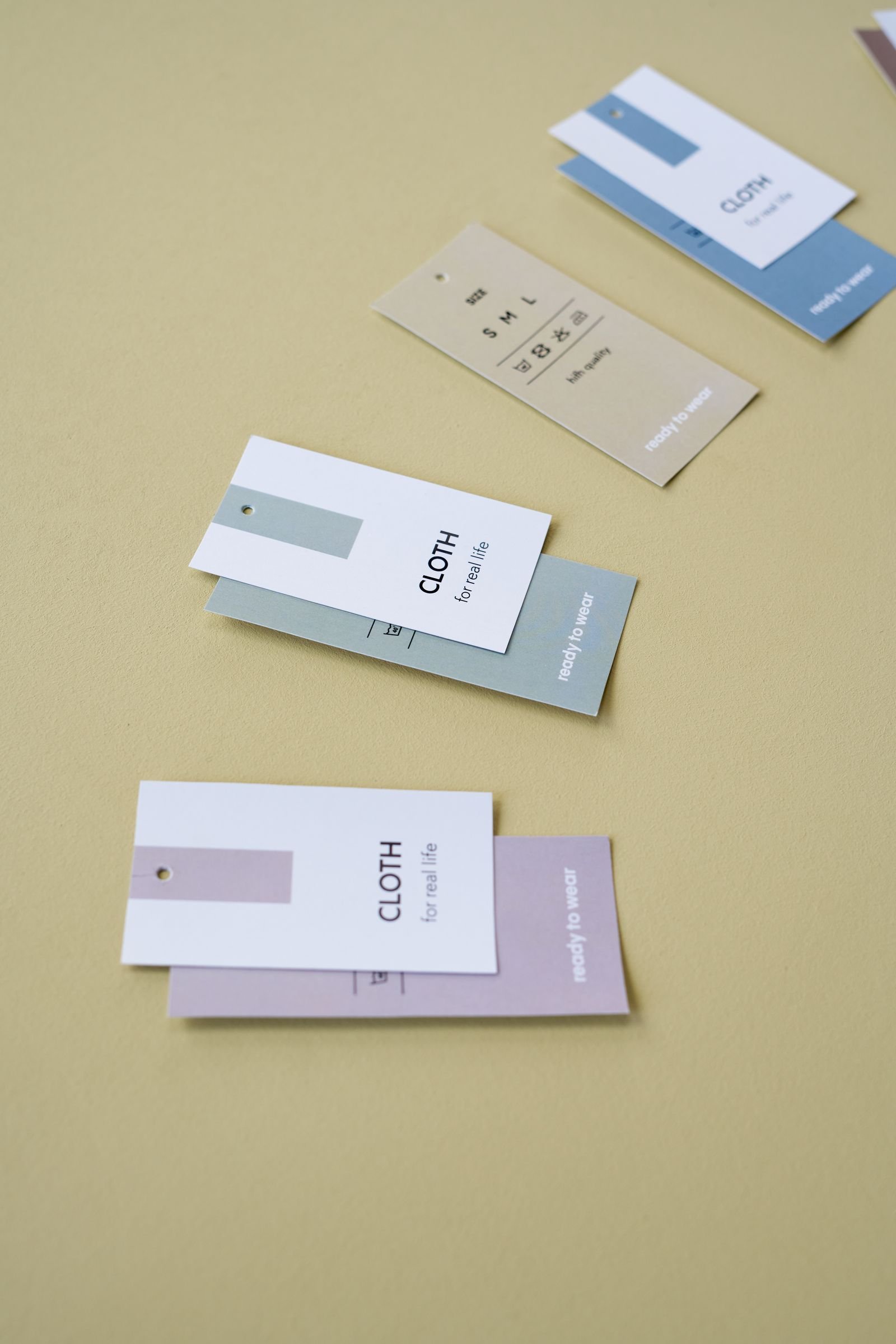 Several printed clothing hang tags arranged on a pale yellow surface