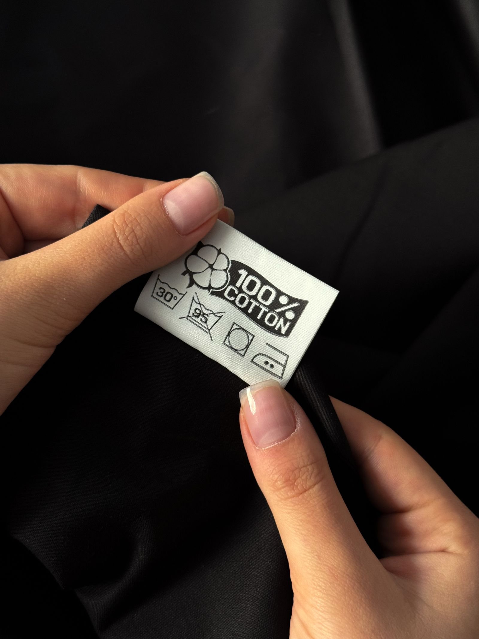 Handen onderzoeken een fysieke katoenen kledingetiket met barcode informatie