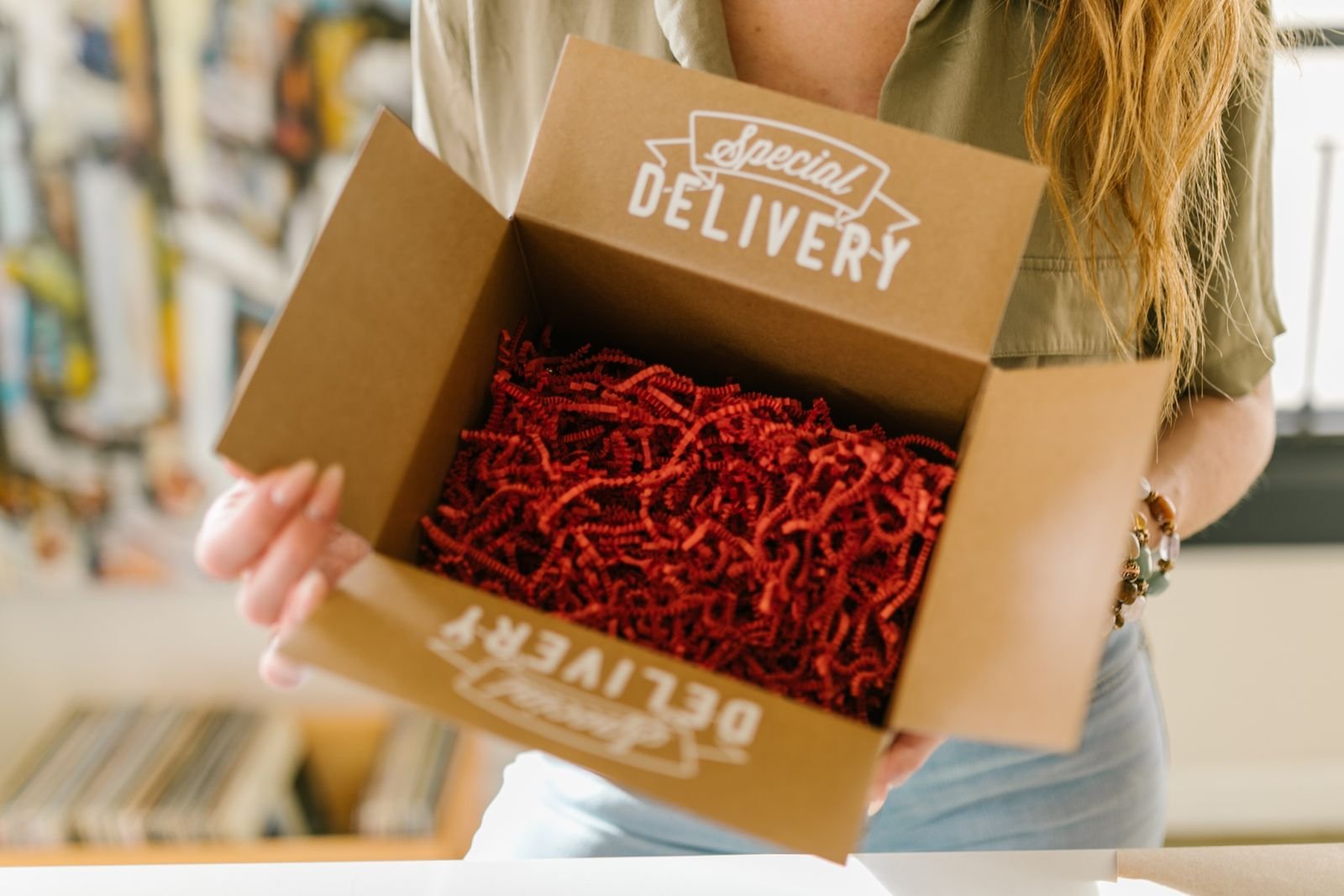 Person, die eine mit rotem Knitterpapier gefüllte Versandbox öffnet