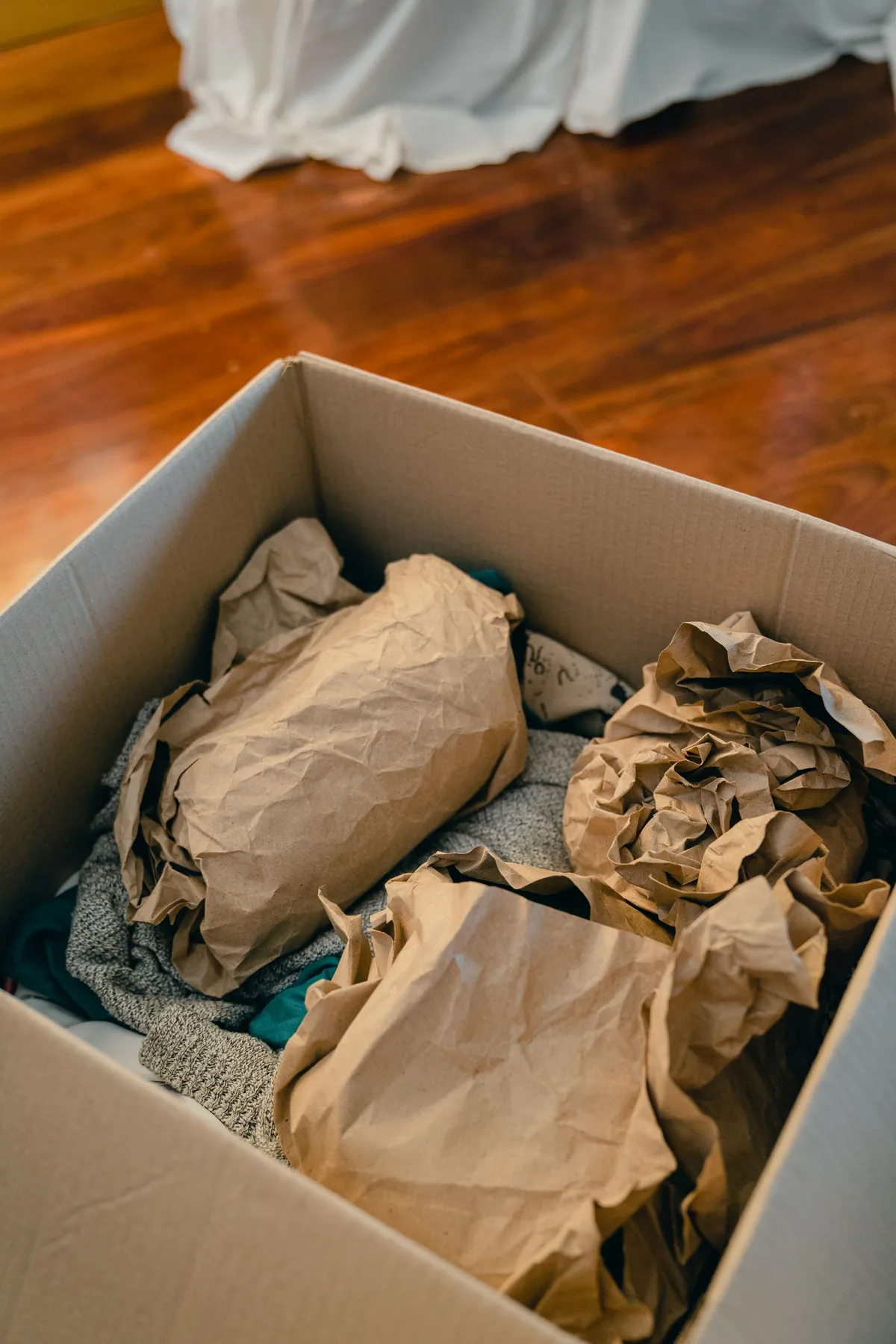 Open cardboard box containing clothing wrapped in brown packing paper