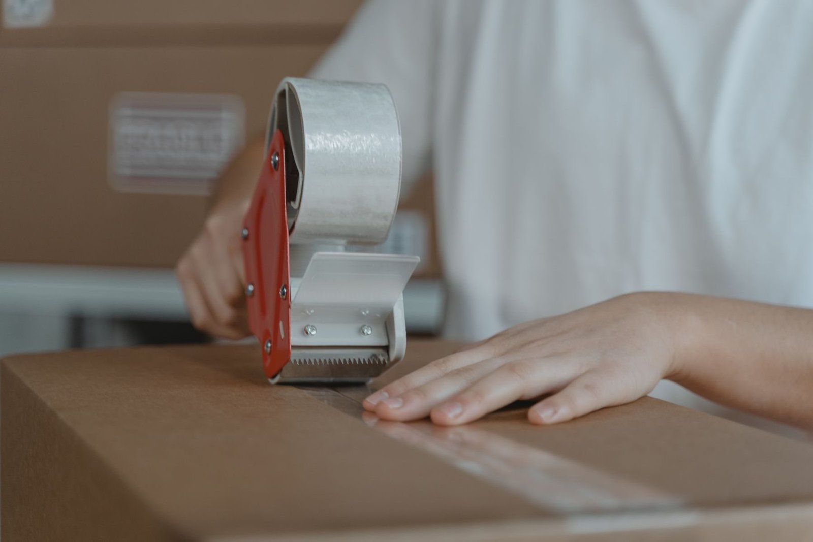 Person, die das Verpackungsband über die Mittelnaht eines Wellpappekartons aufbringt