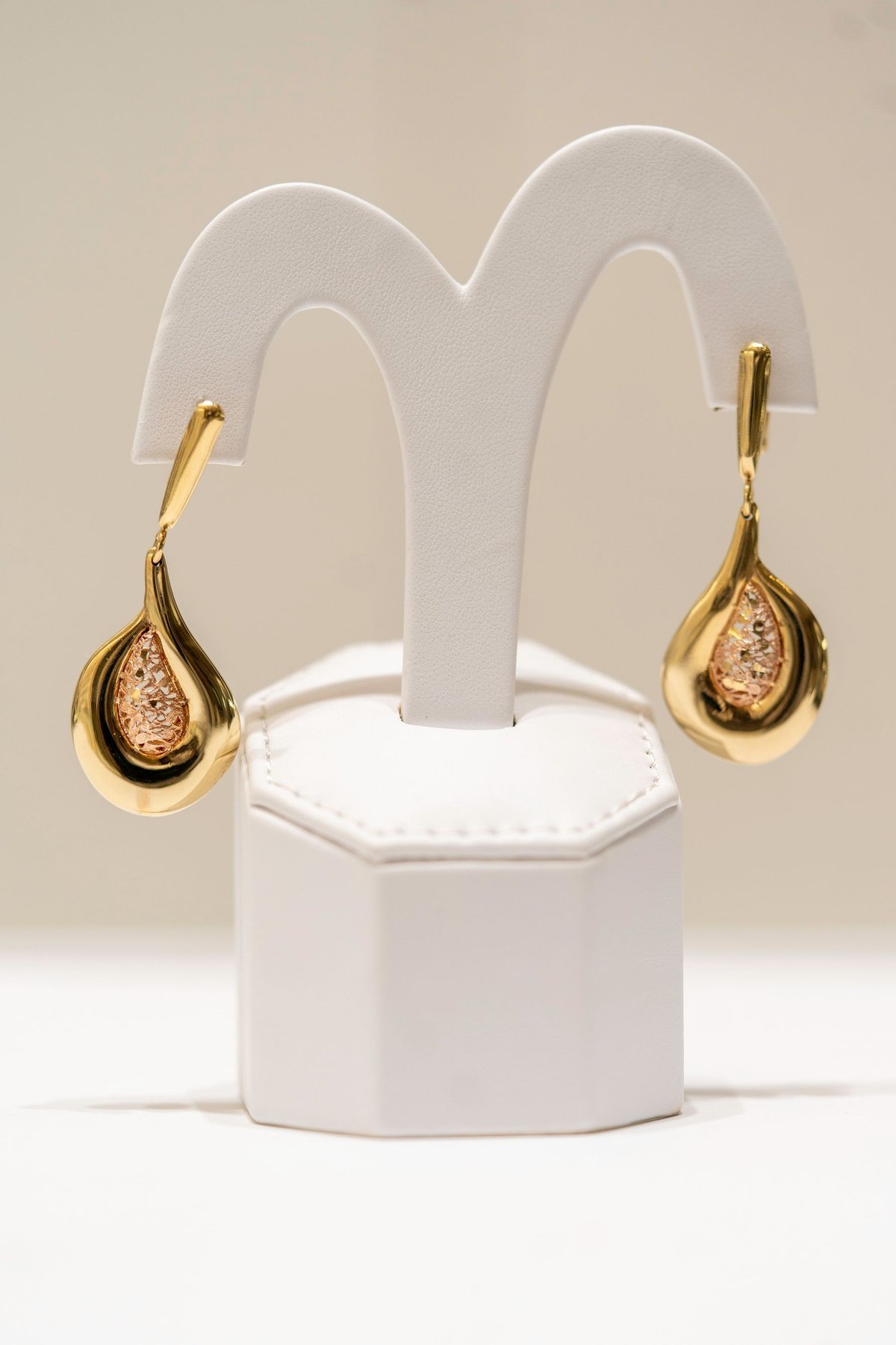 Gold baumelnde Ohrringe auf einem weißen Display-Ständer, die sichtbare Form und Falllänge darstellen