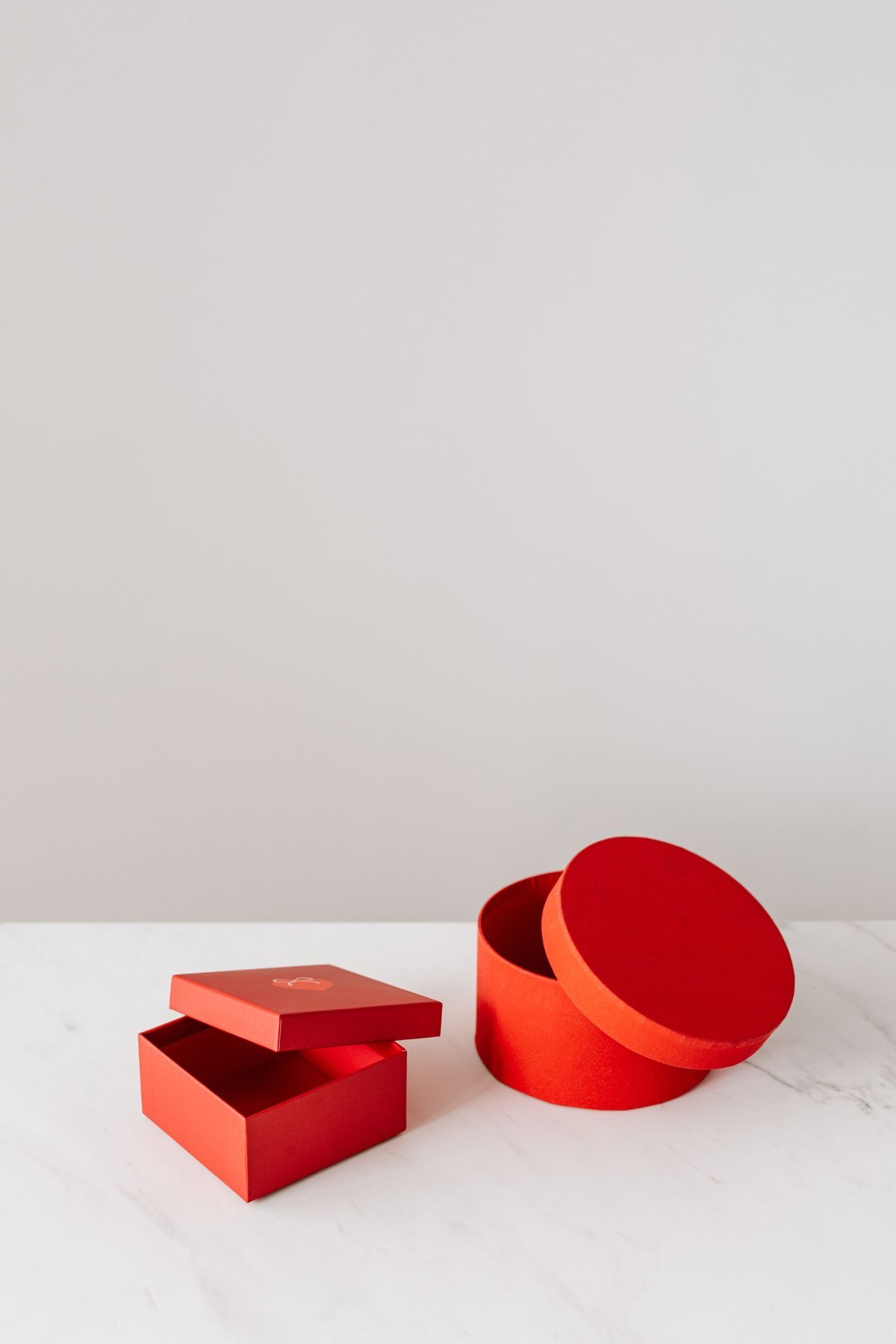 Empty square and round red presentation boxes with their separate lids on a white surface
