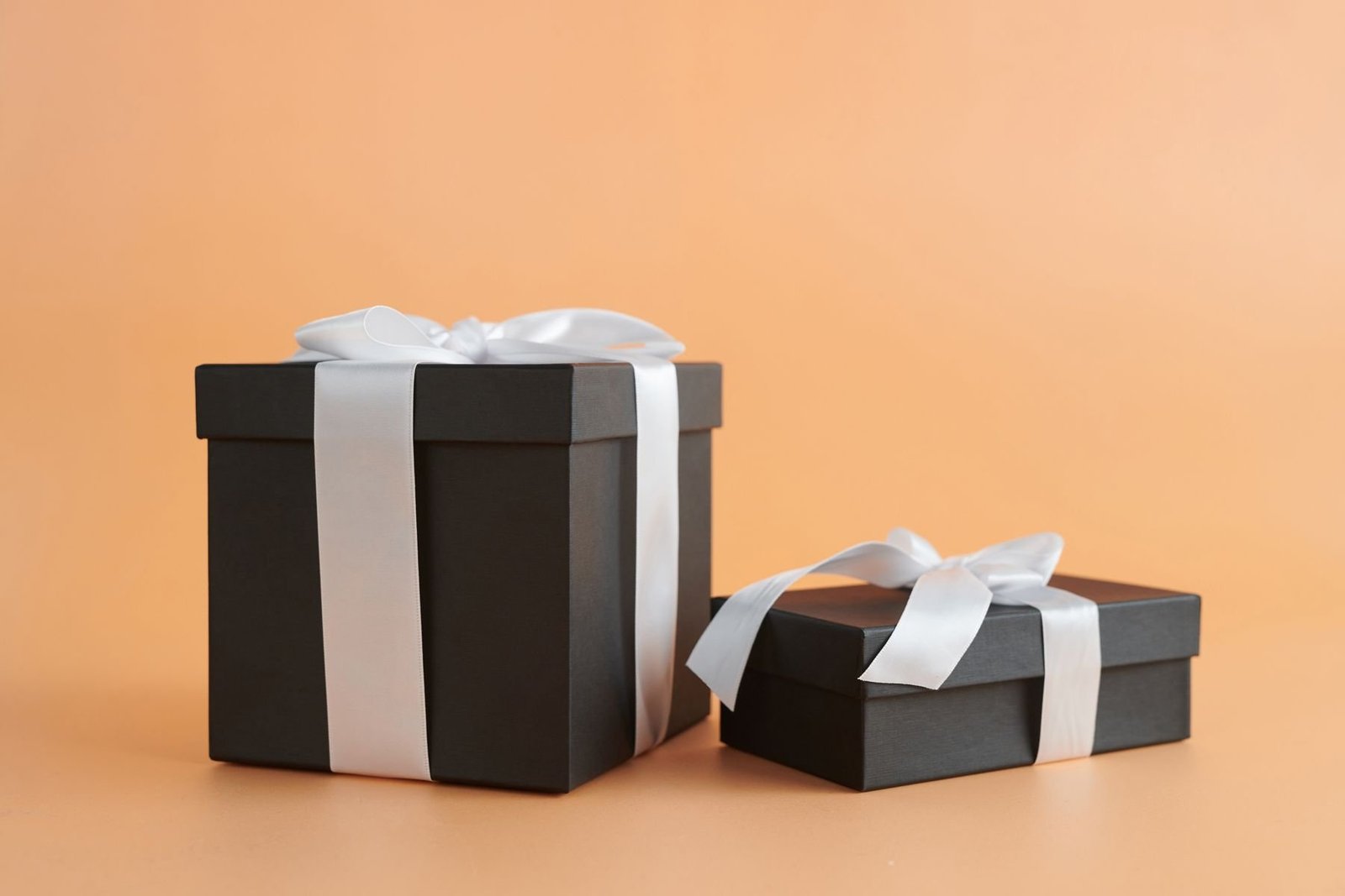 Two black gift boxes with contrasting white ribbons, illustrating coordinated presentation finishes