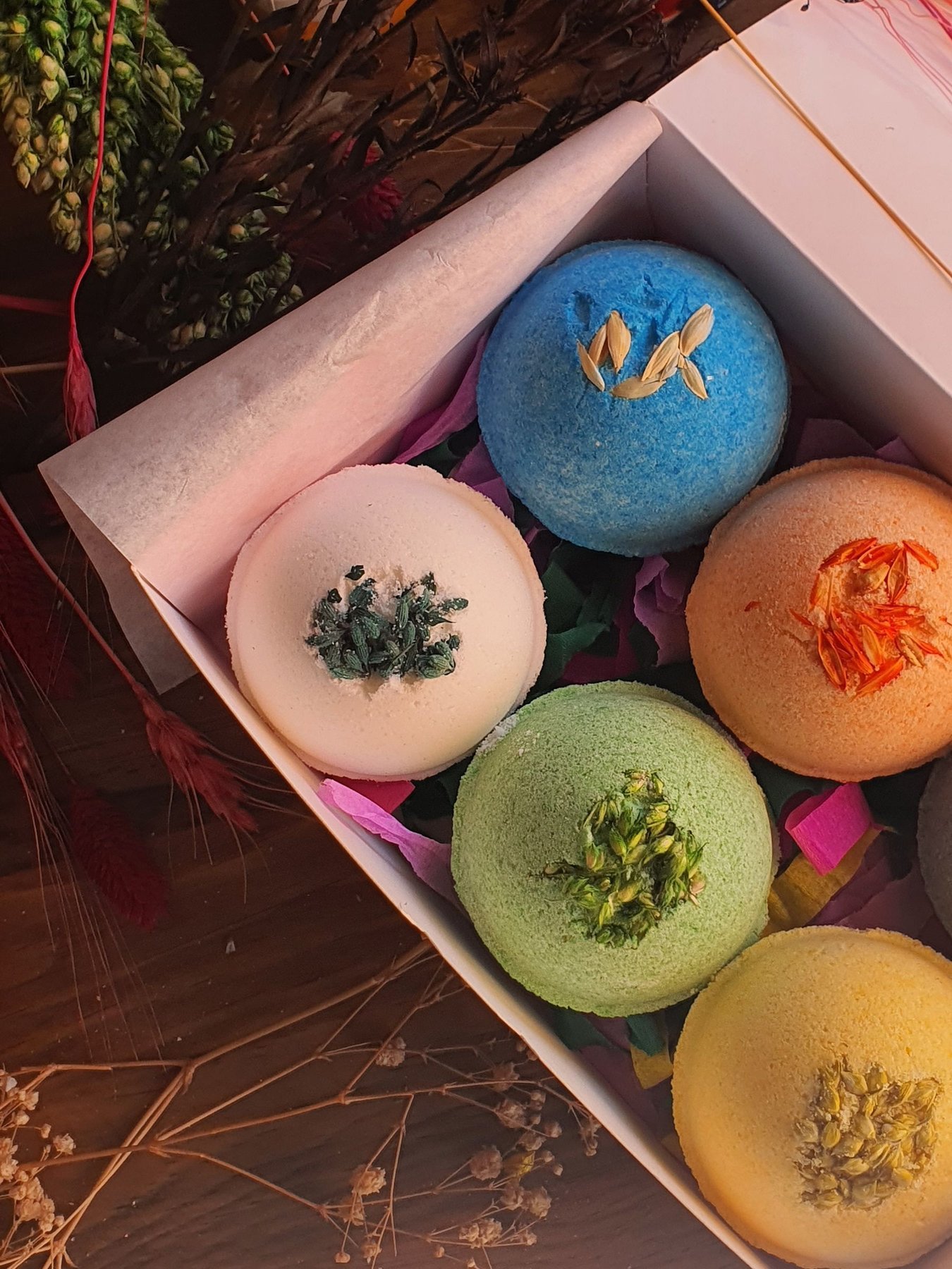 Five colourful bath products arranged inside a pink presentation box