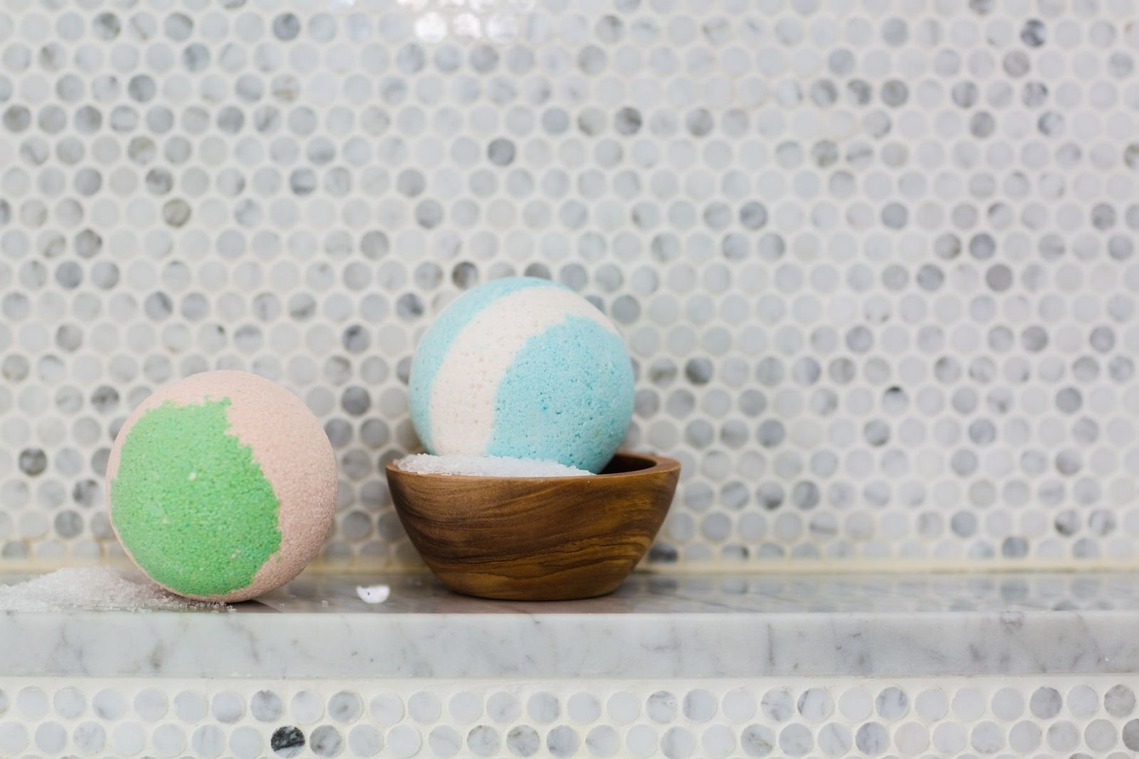 Pastel spherical bath bombs arranged on a marble surface beside a wooden bowl