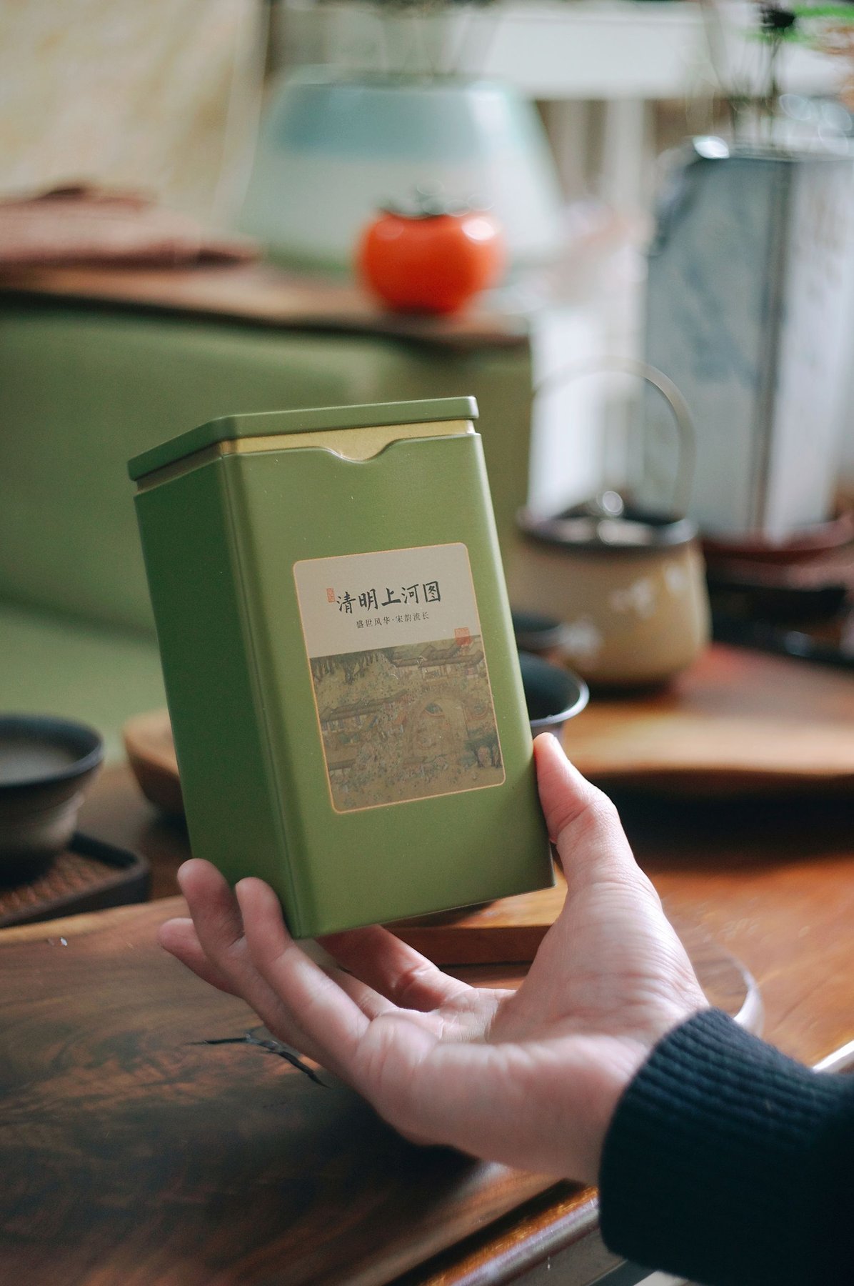 A person holding a green tea tin beside a tea service