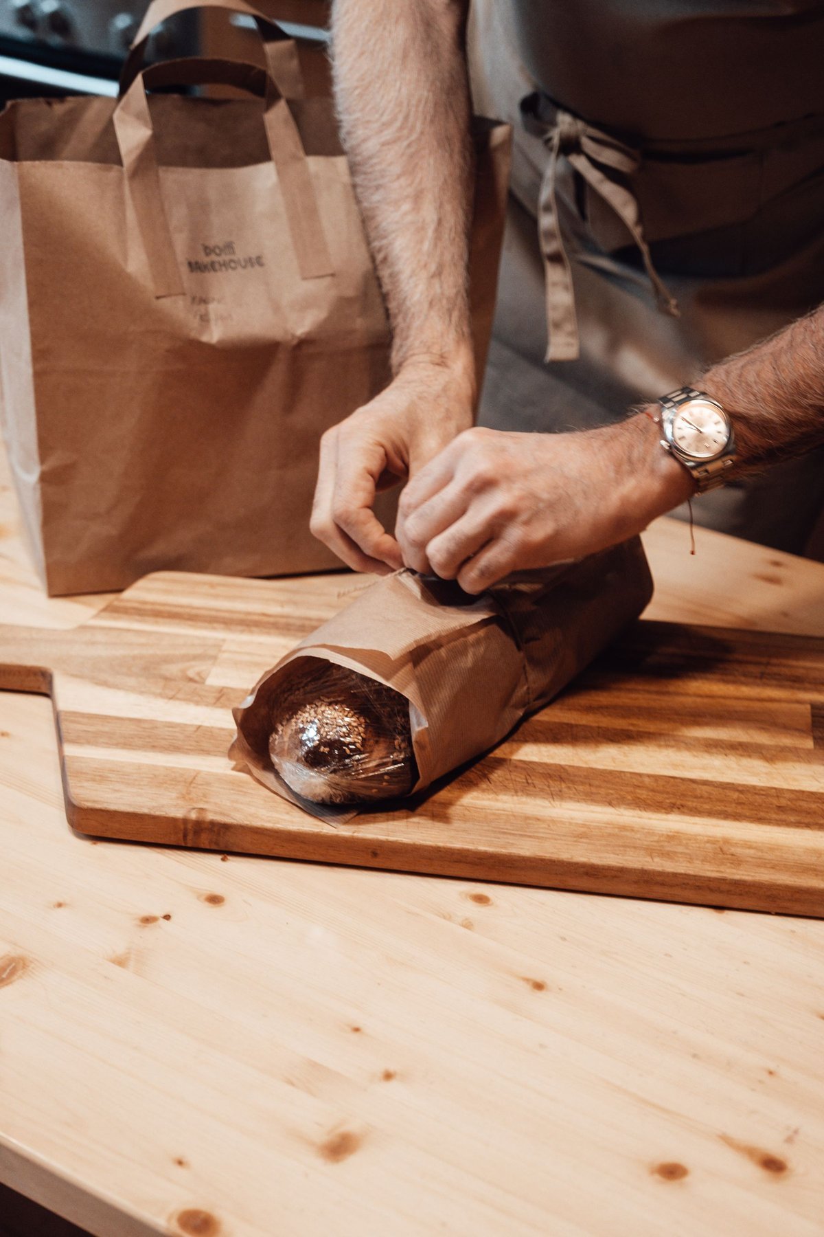 A baker folding paper around a loaf of bread at a packing counter