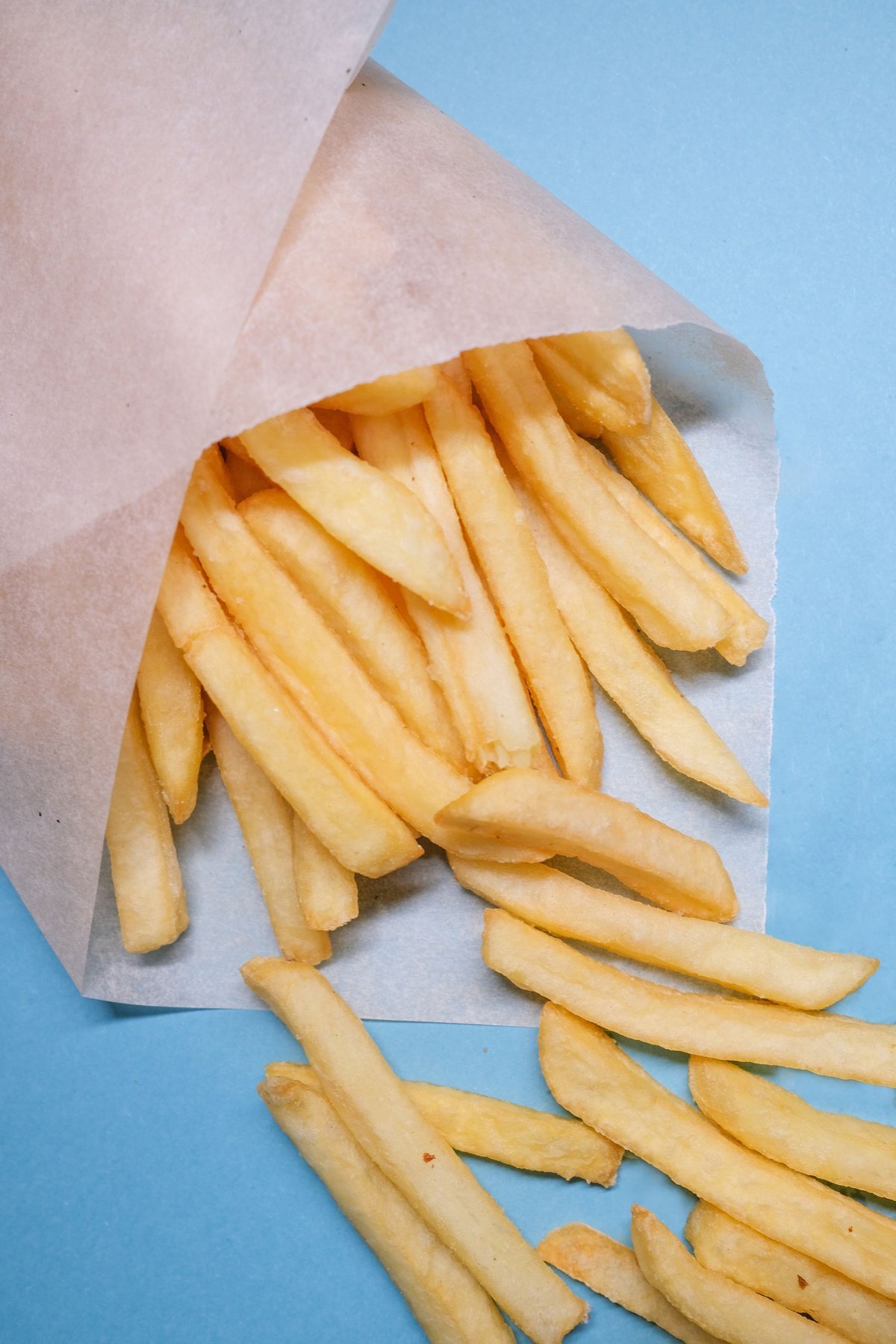 French fries spilling from a folded paper wrapper on a blue surface
