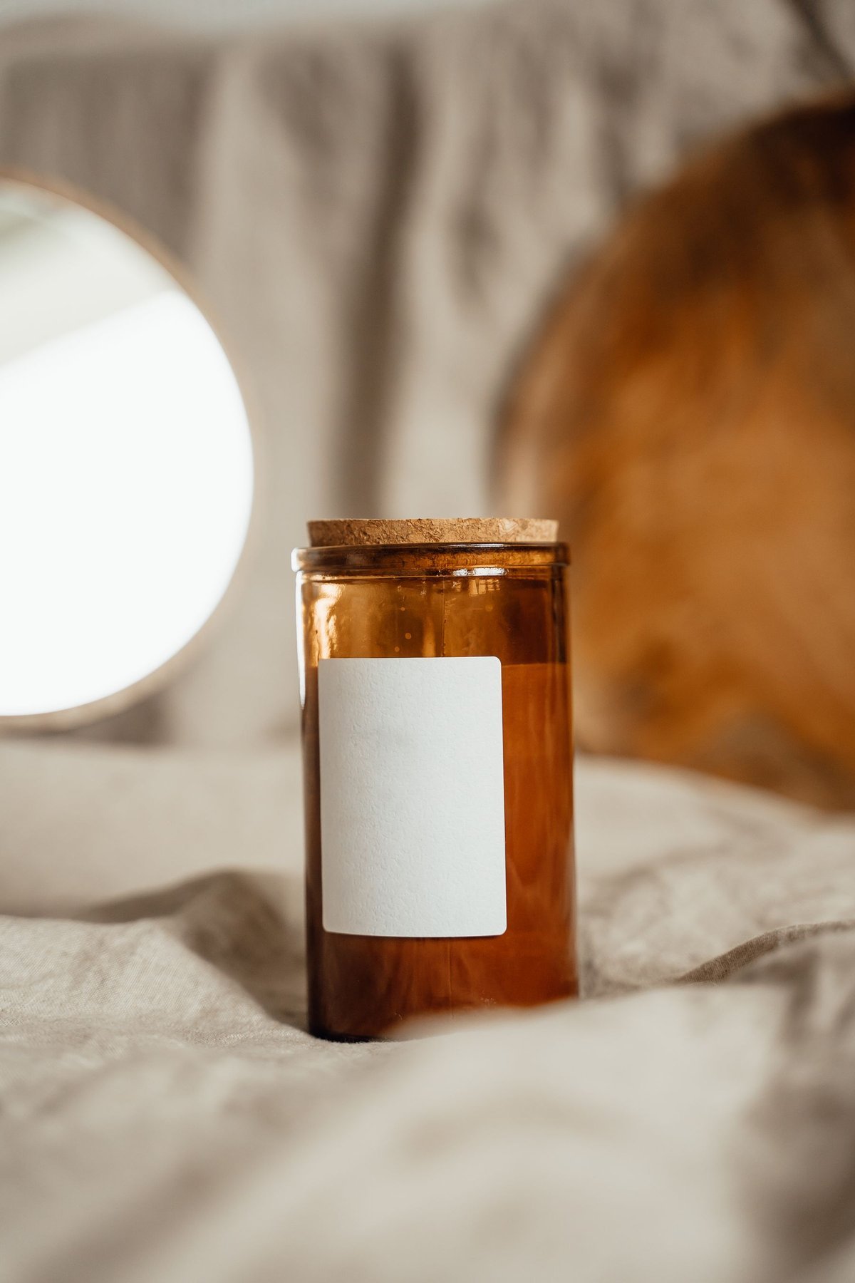 A brown glass candle jar with a blank rectangular label and cork lid