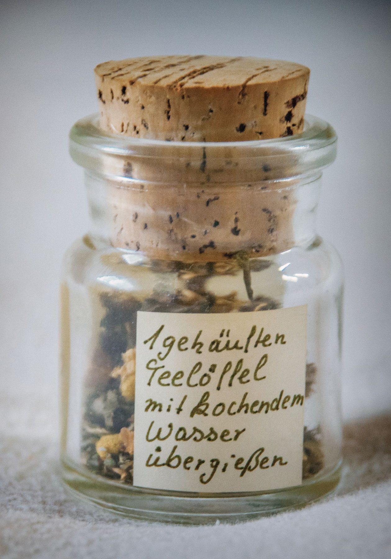 A glass herb jar with a handwritten paper label and cork stopper