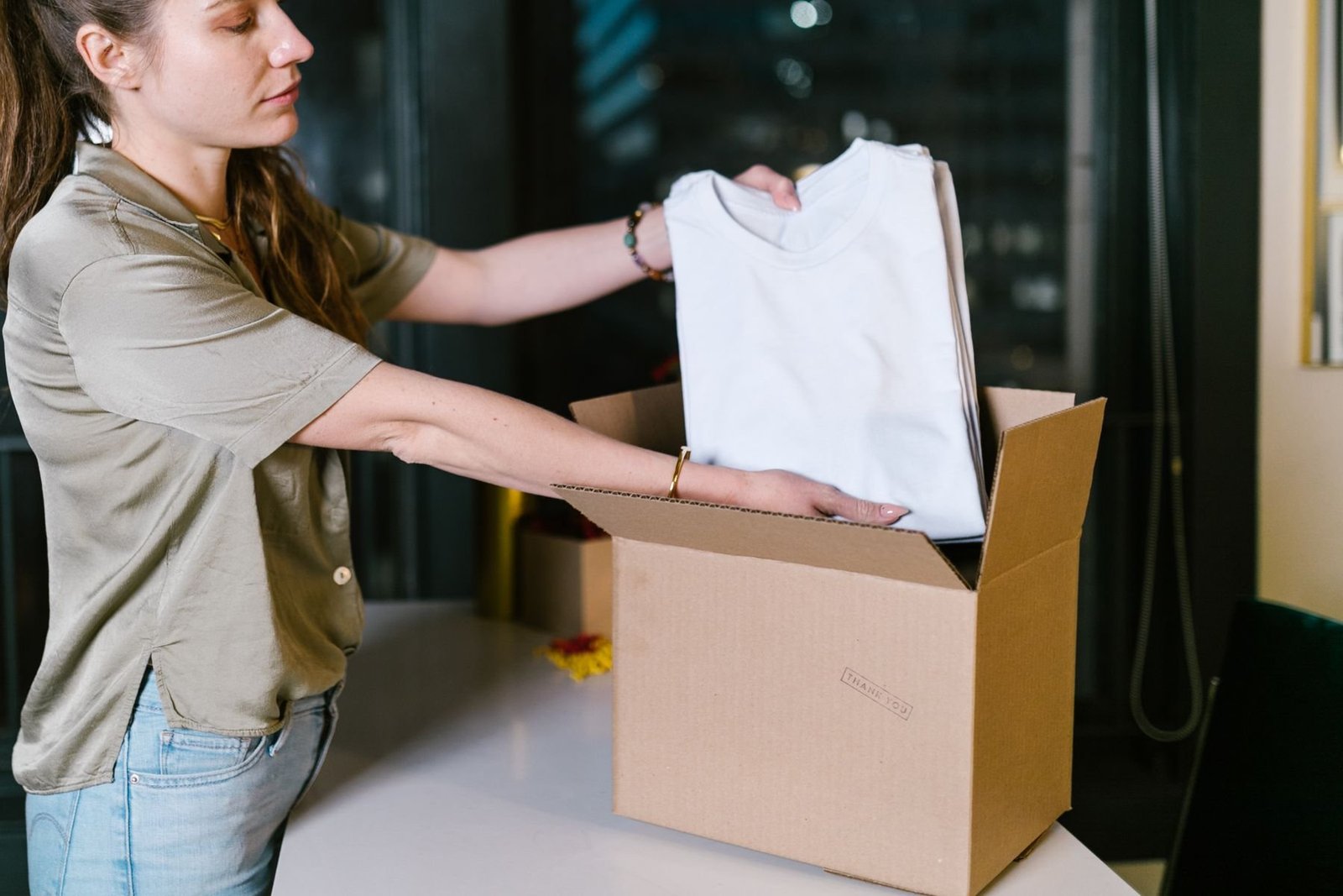 A woman placing a folded shirt into a cardboard box