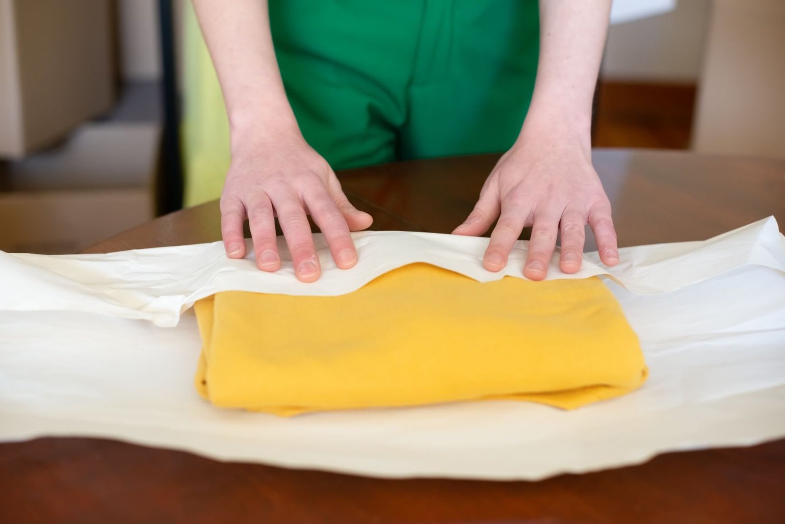 Hands folding white tissue paper around a yellow garment