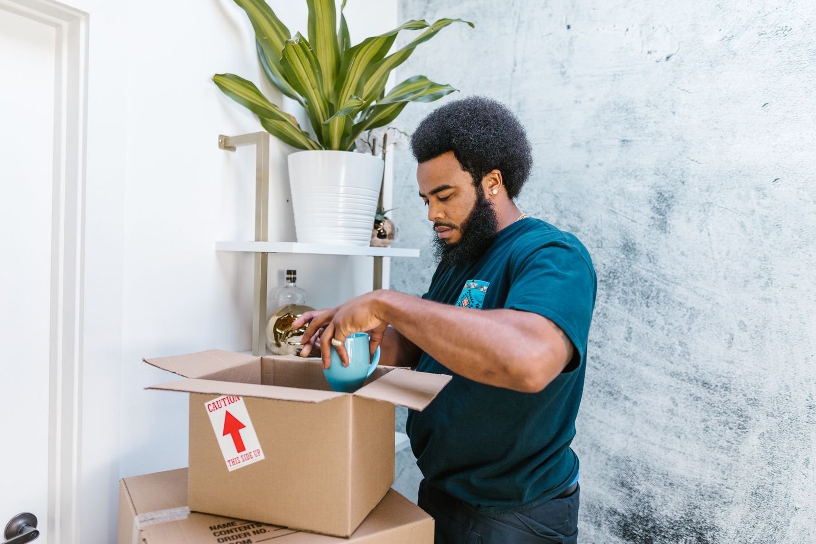 A person wrapping a blue ceramic mug beside an open cardboard box