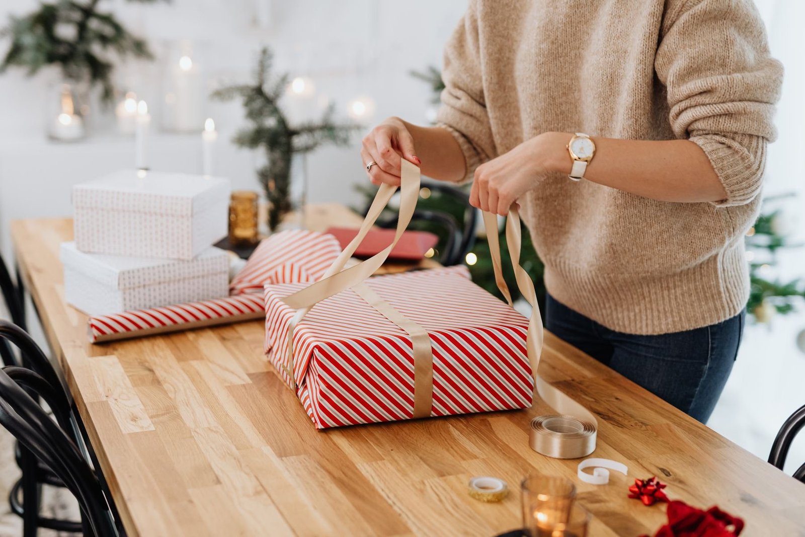 Hands tying a ribbon around a striped Christmas gift on a packing table