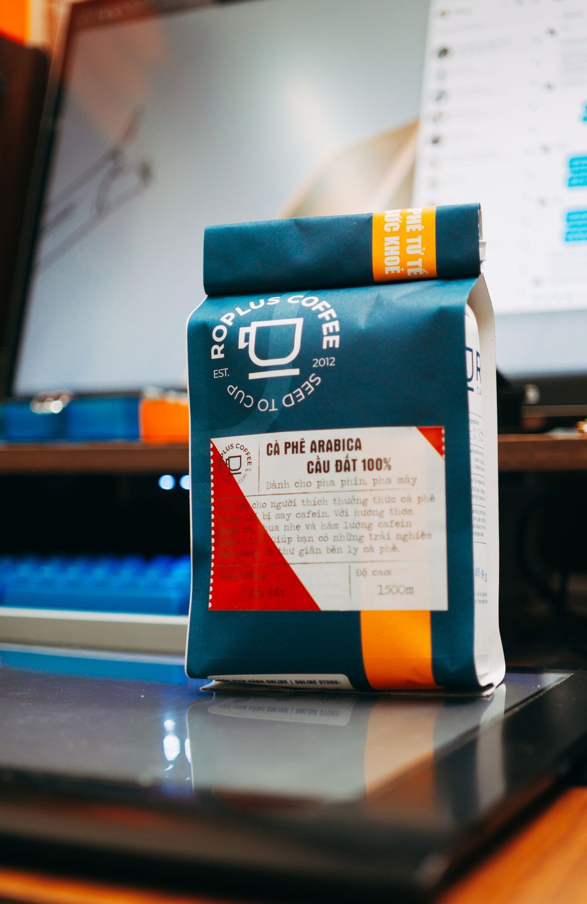 A blue printed coffee pouch standing beside a laptop