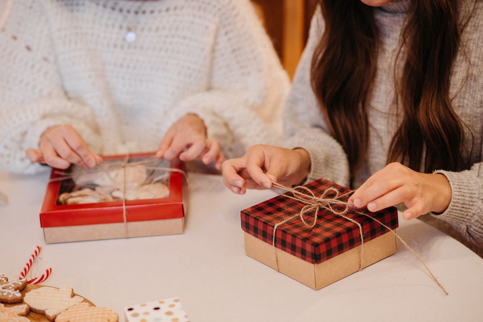 People tying twine around red cookie gift boxes at a table