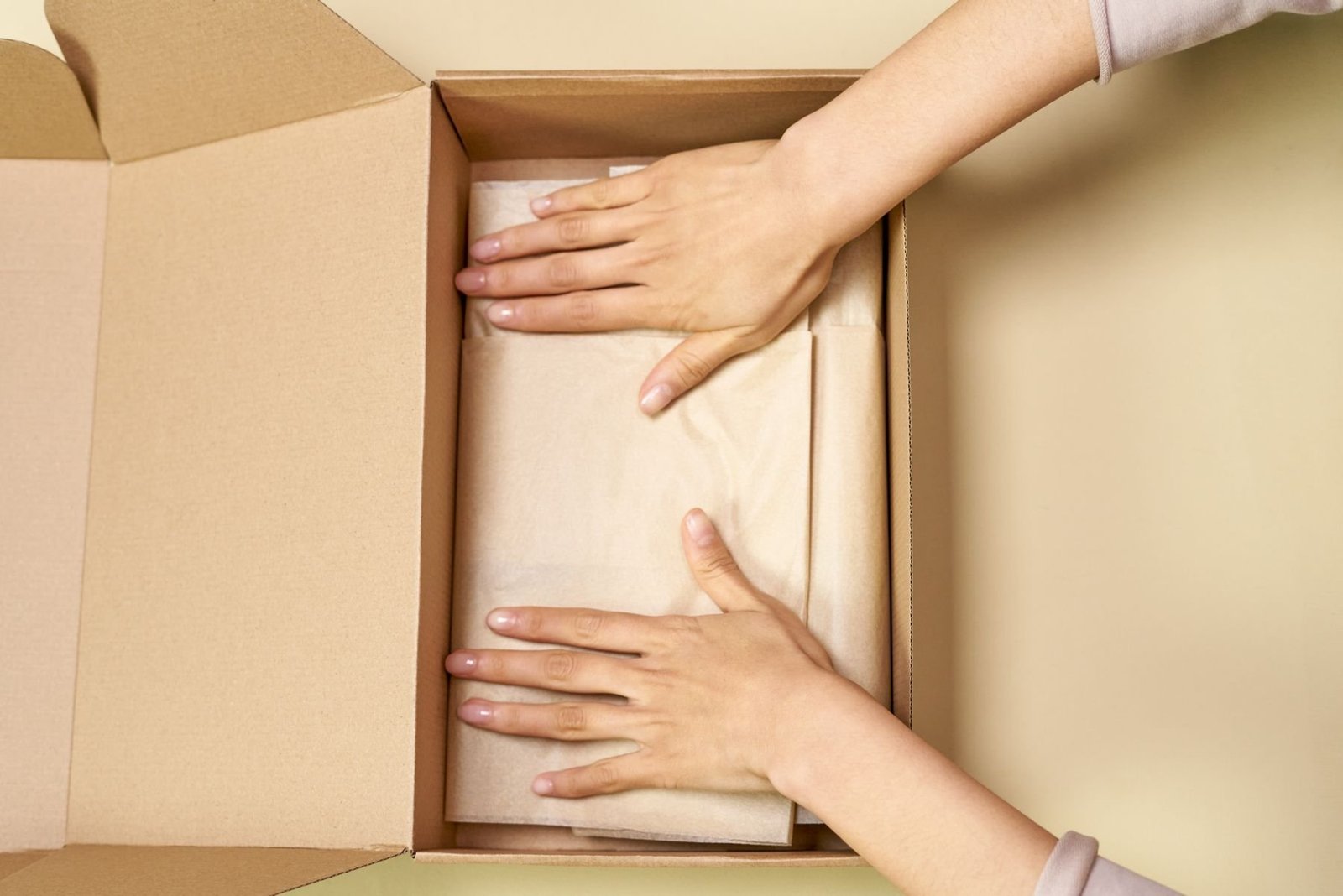 Hands arranging brown paper around the contents of an open corrugated box