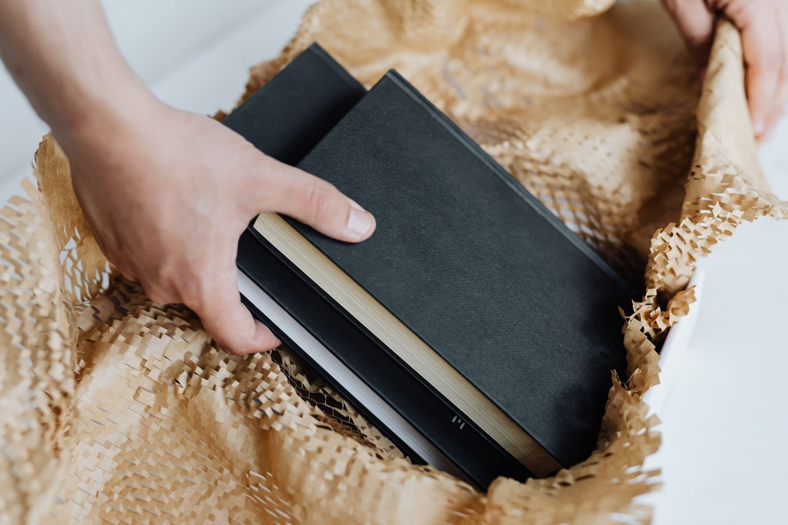 Hands placing black notebooks in a white box with shredded paper fill