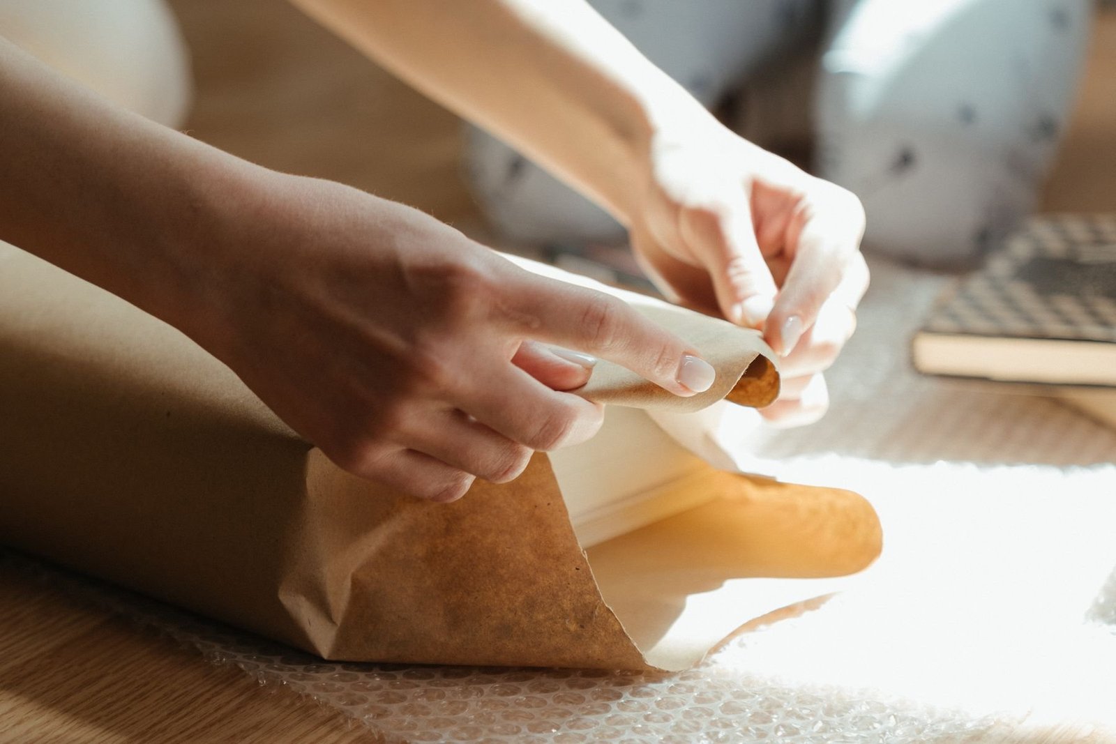 Hands folding brown paper around an item in sunlight