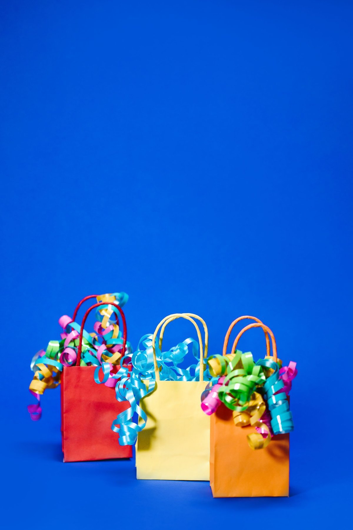 Three colorful paper gift bags with decorative ribbons against blue