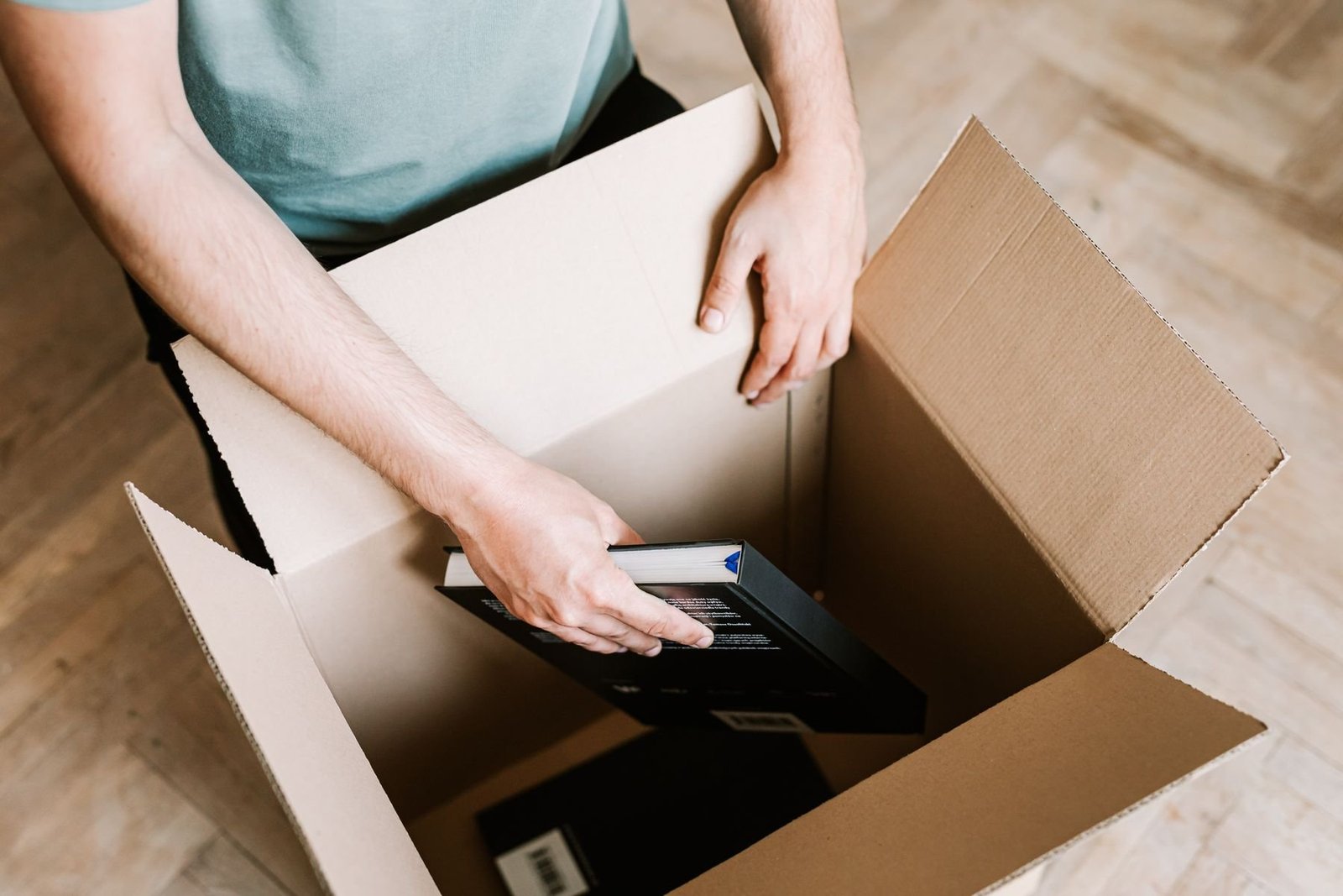 Top view of hands arranging hardcover books in an open carton