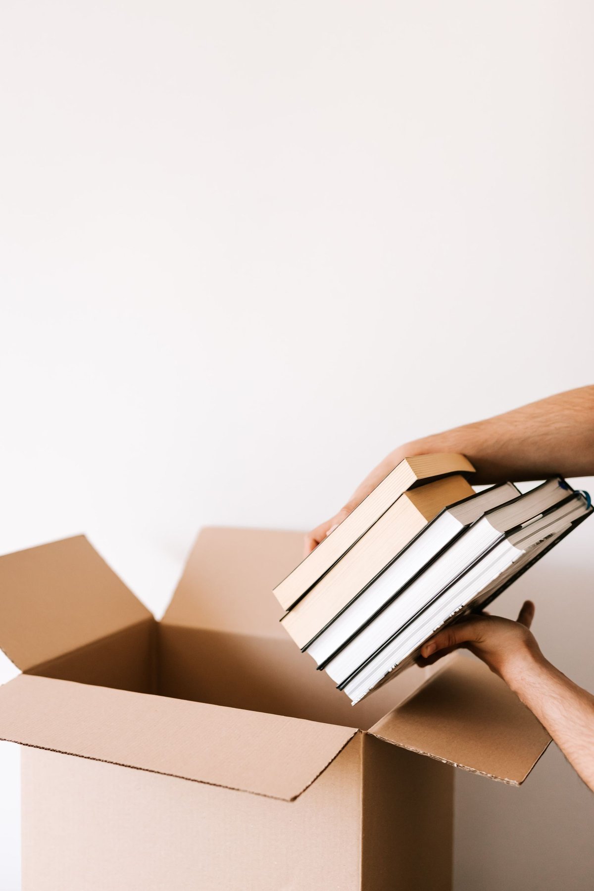 Hands lowering a stack of books into a cardboard box