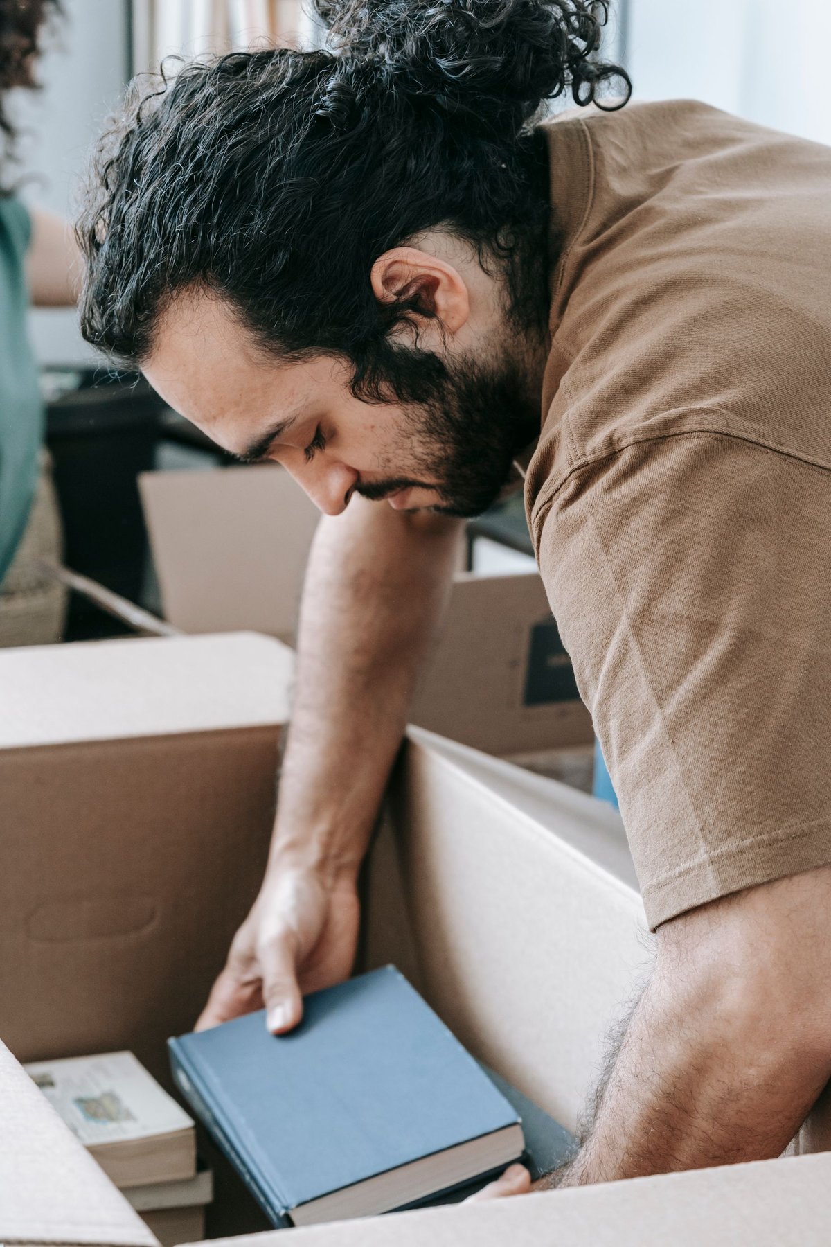 A man placing books in a cardboard box beside a bookshelf