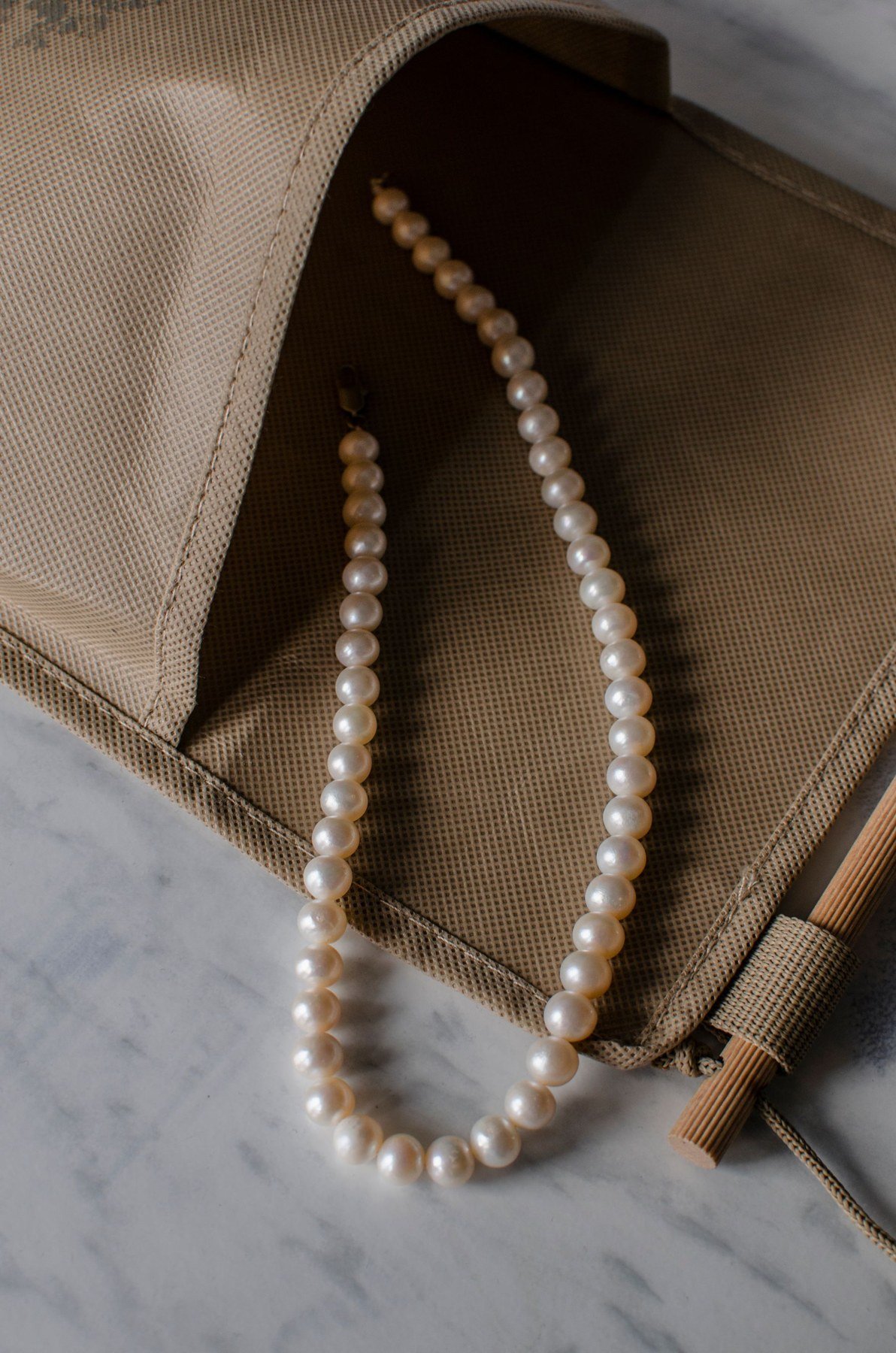 A strand of pearl beads resting across a beige fabric bag